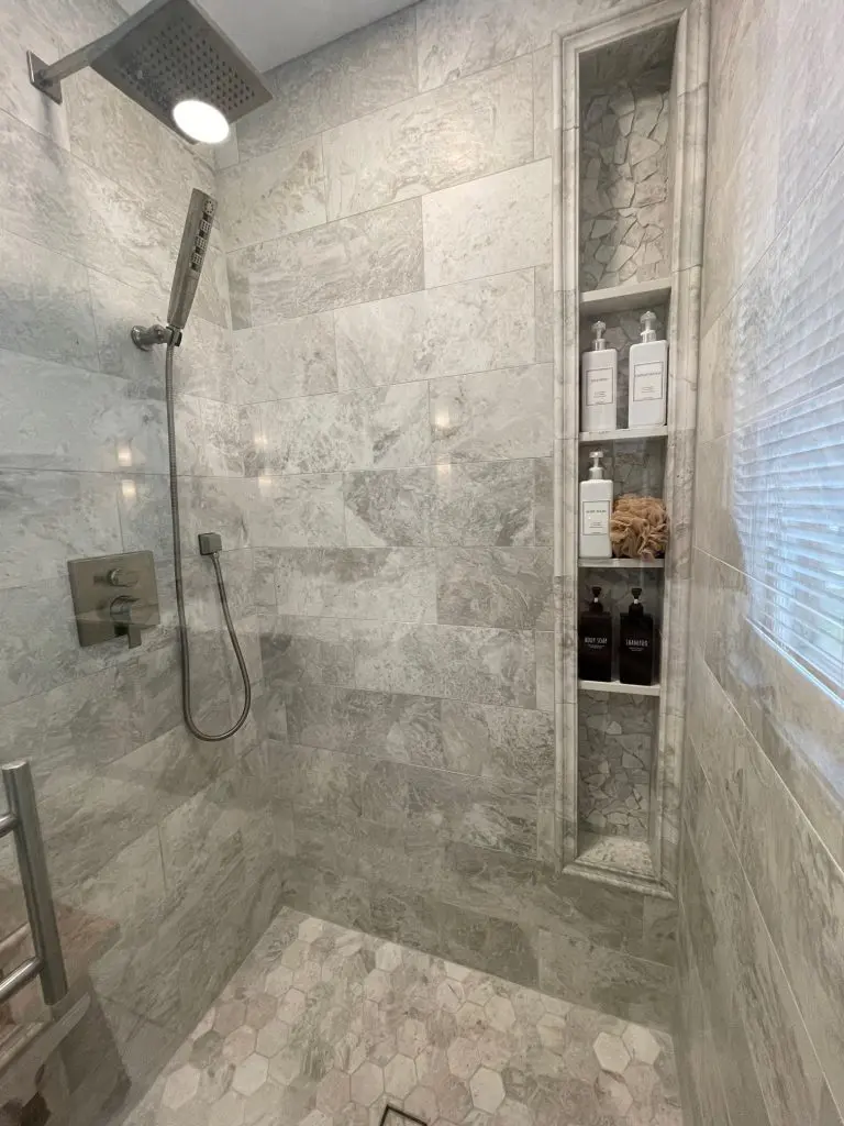 Remodeled bathroom with walk in shower featuring modern tile and built in storage.