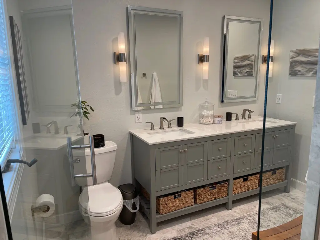 Modern remodeled bathroom with grey cabinets, white countertops and dual mirrors.