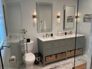 Modern remodeled bathroom with grey cabinets, white countertops and dual mirrors.